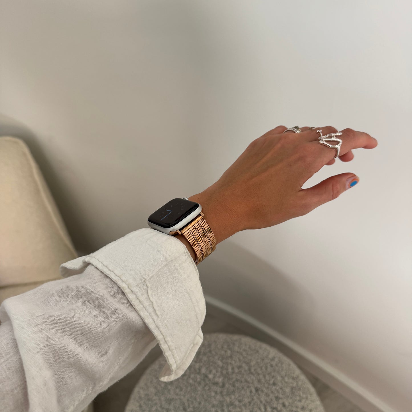 Rose gold flat woven Apple Watch band worn on a wrist with rings on the hand. Waterproof stainless steel iWatch strap, compatible with Apple Watch 38mm to 49mm, Series 1-11, SE and Ultra