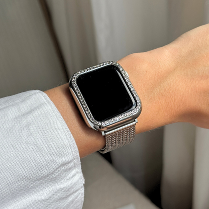 Smartwatch with a decorative band on a wrist against a neutral background with a silver rhinestone apple watch case