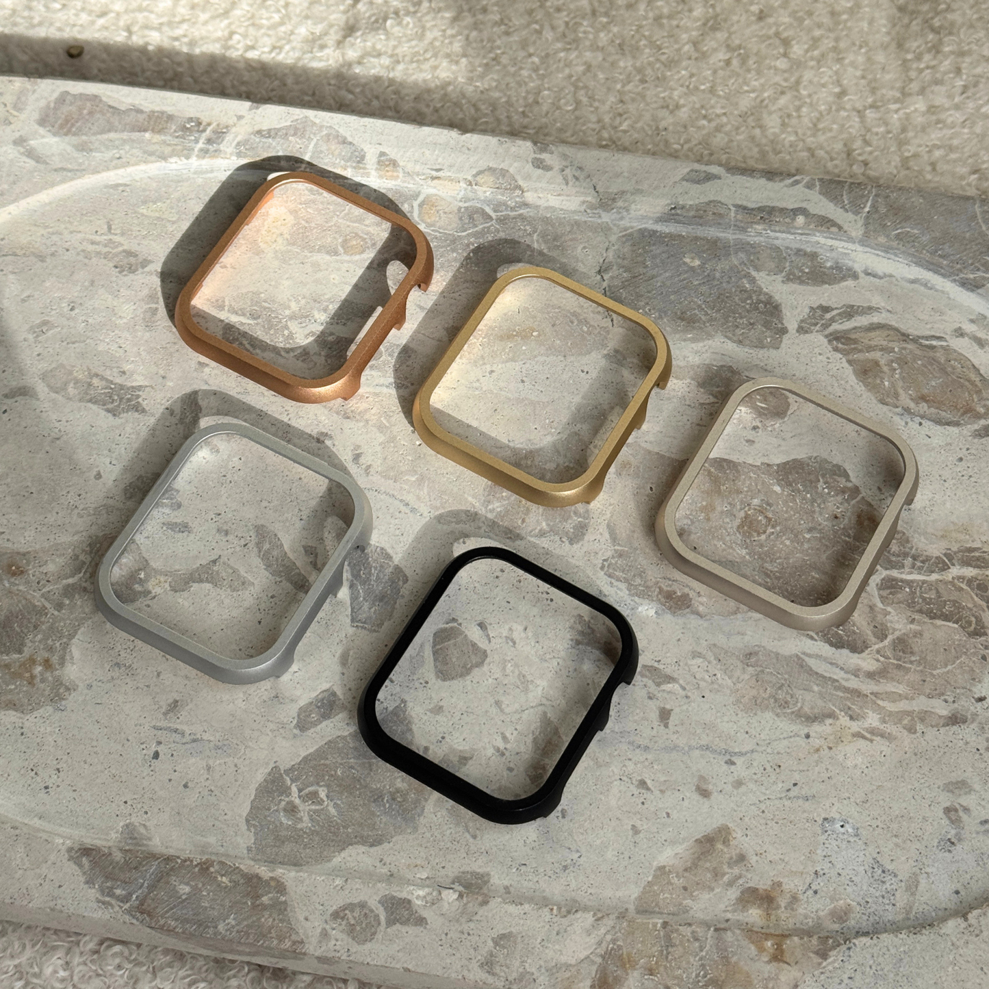 Rose gold, gold, starlight, silver and black stainless steel Apple Watch case covers arranged on a marble tray. Durable protective bumpers, available for Apple Watch 38mm to 49mm, Series 1-11, SE and Ultra