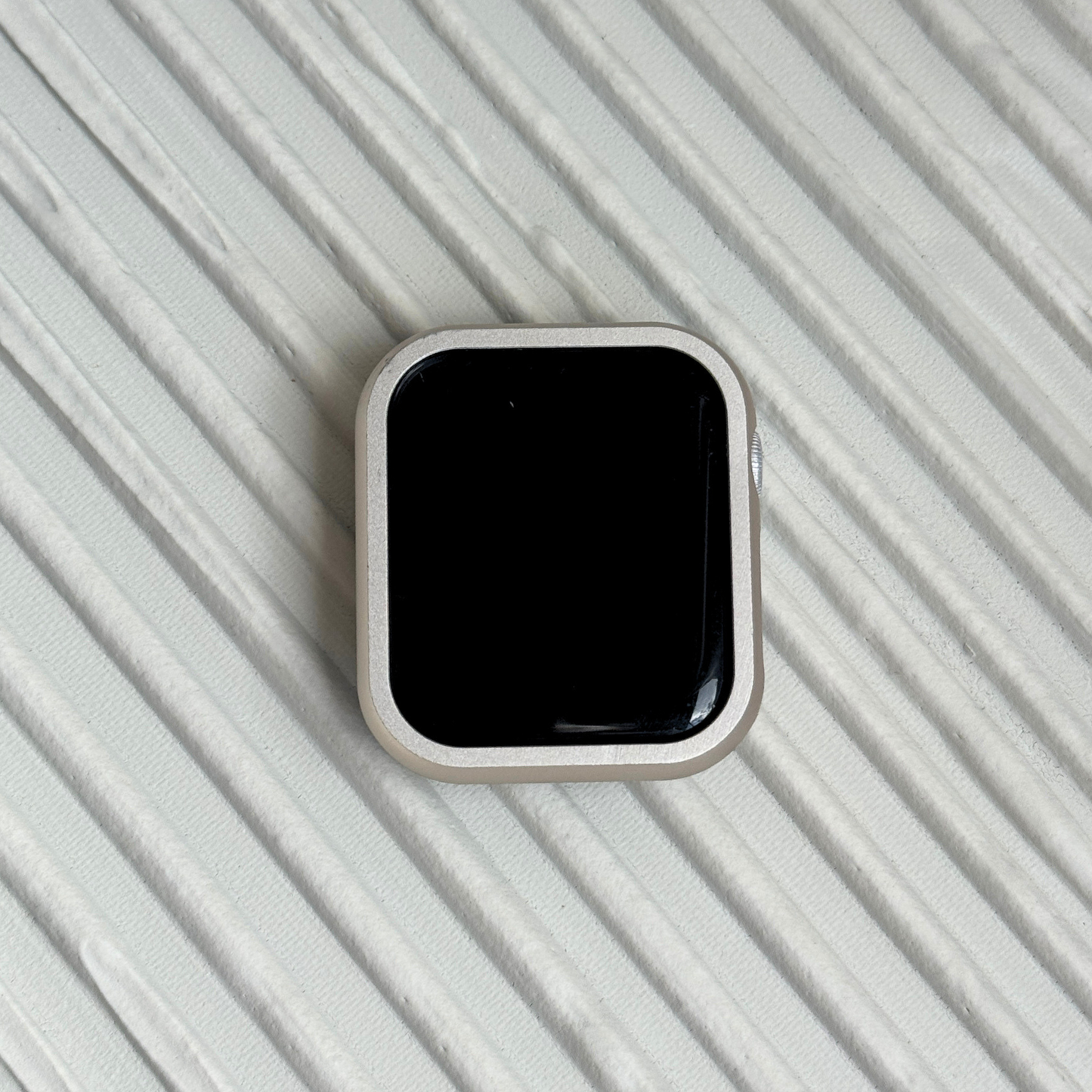 Starlight stainless steel Apple Watch case cover shown on a ribbed white surface. Refined protective bumper, available for Apple Watch 38mm to 49mm, Series 1-11, SE and Ultra