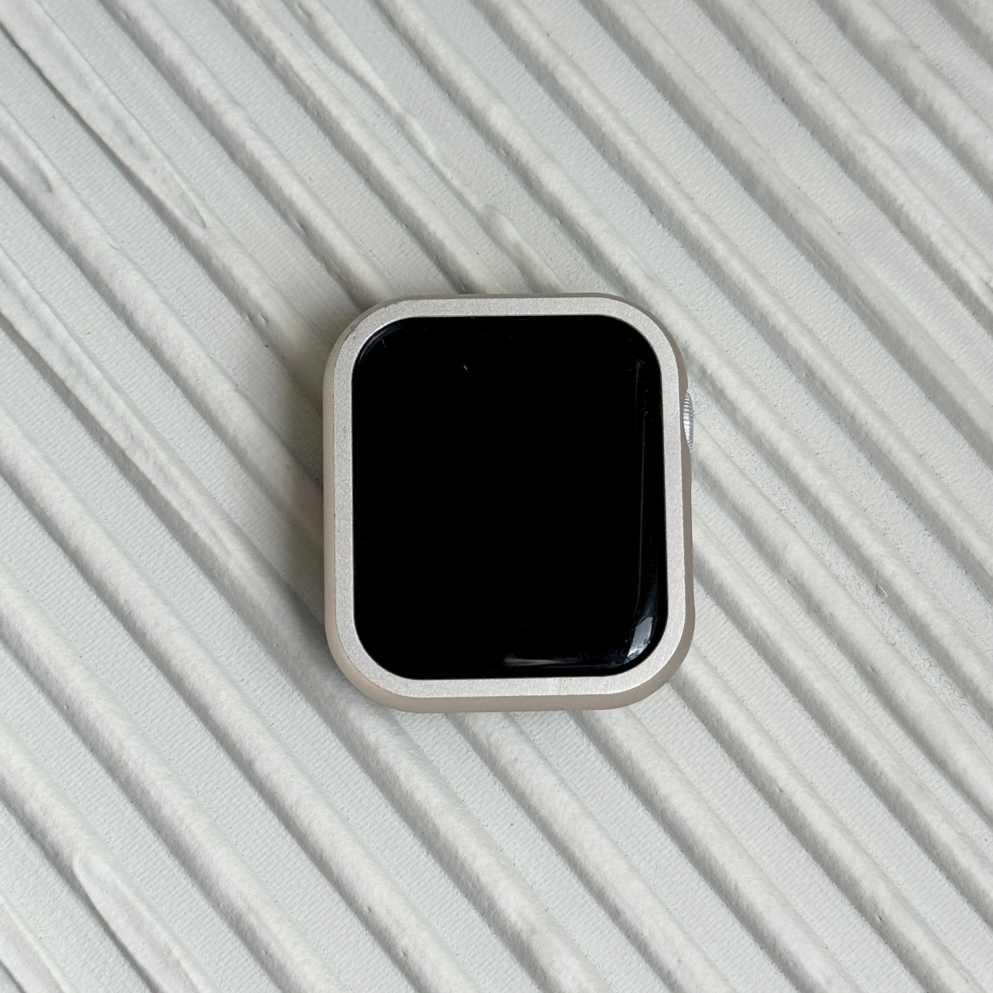 Starlight stainless steel Apple Watch case cover shown on a ribbed white surface. Refined protective bumper, available for Apple Watch 38mm to 49mm, Series 1-11, SE and Ultra