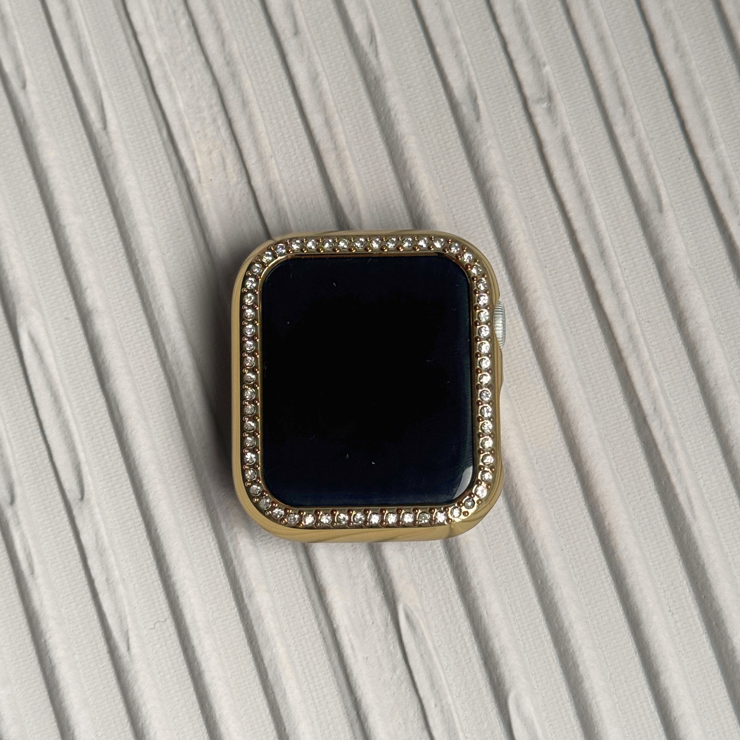 Gold rhinestone apple watch case on a textured surface