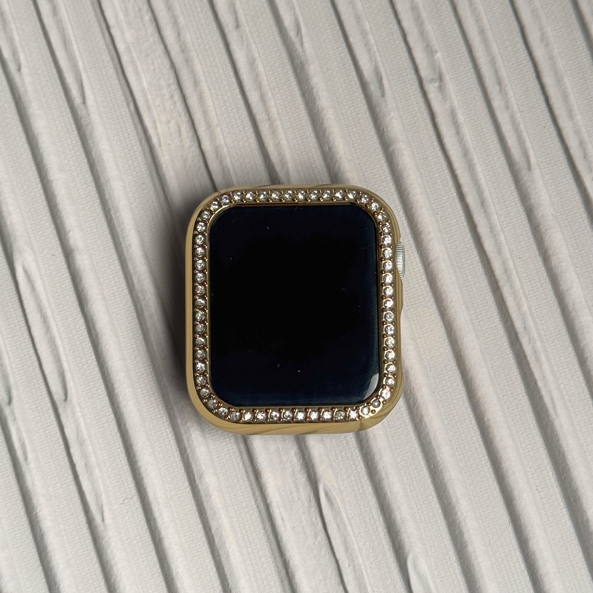Gold rhinestone apple watch case on a textured surface