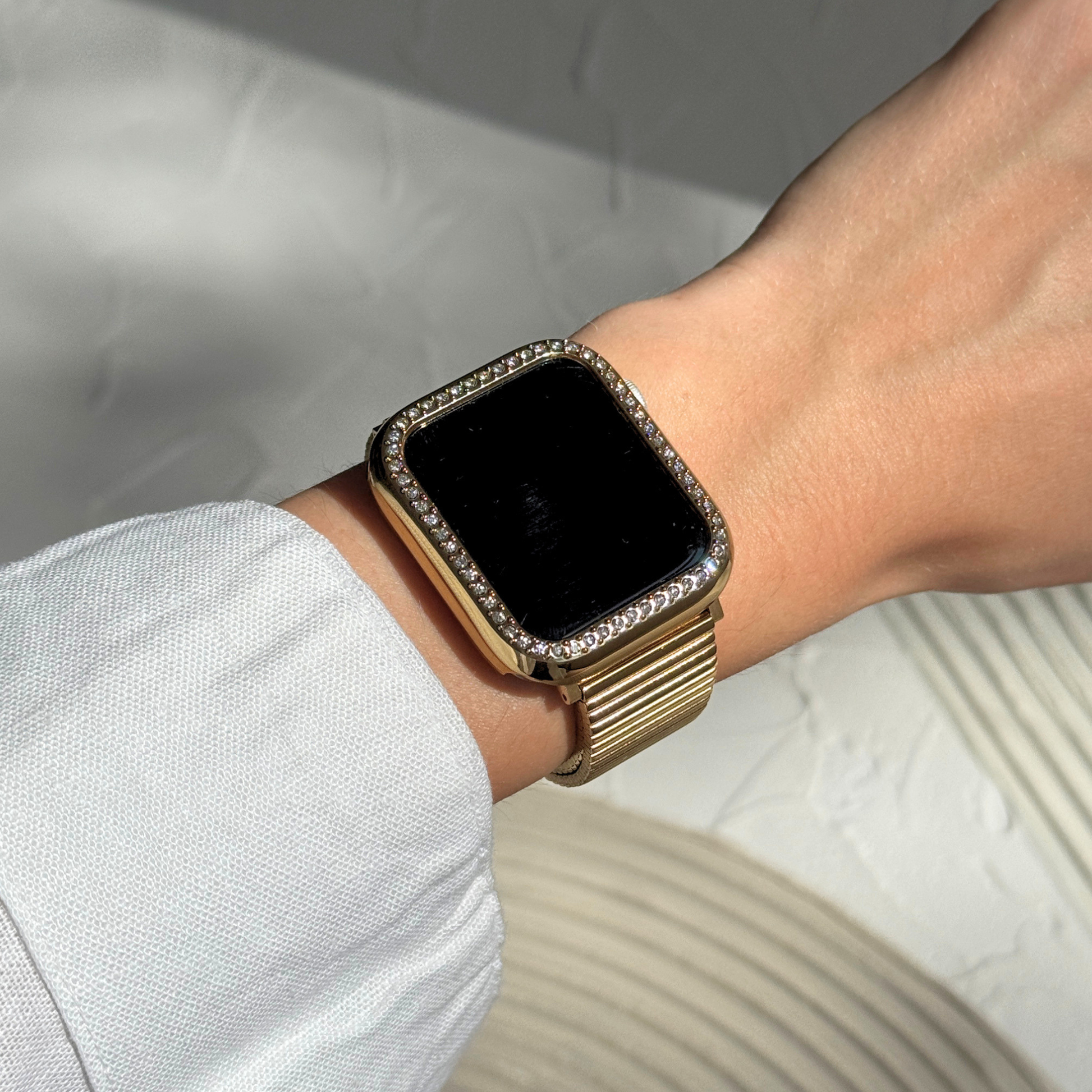 Gold smartwatch with diamond-like accents on a wrist against a neutral background. Gold rhinestone apple watch case