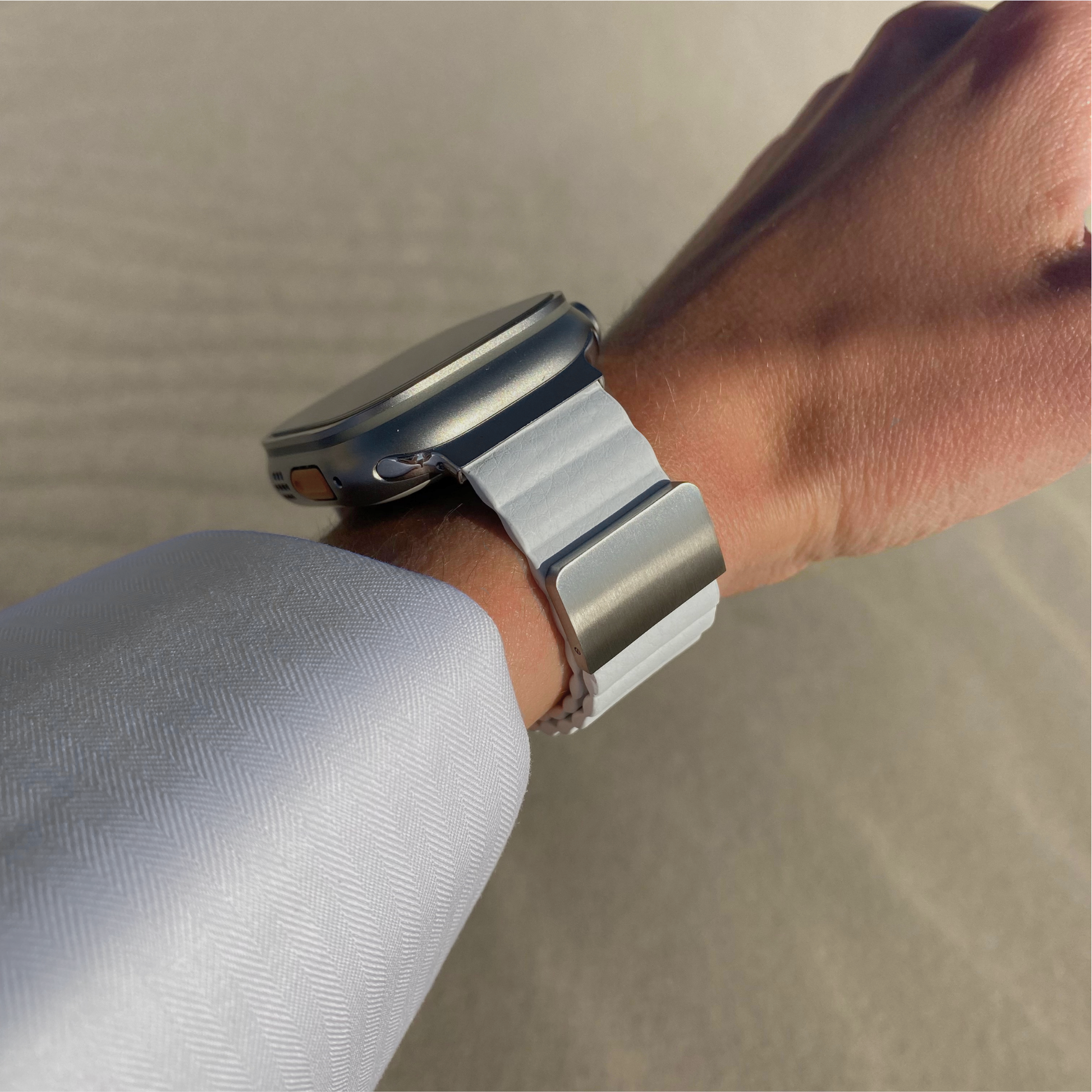 White ribbed vegan leather Apple Watch band worn on a wrist with a pale blue sleeve. Soft magnetic iWatch strap with a hidden magnet, compatible with Apple Watch 38mm to 49mm, Series 1-11, SE and Ultra