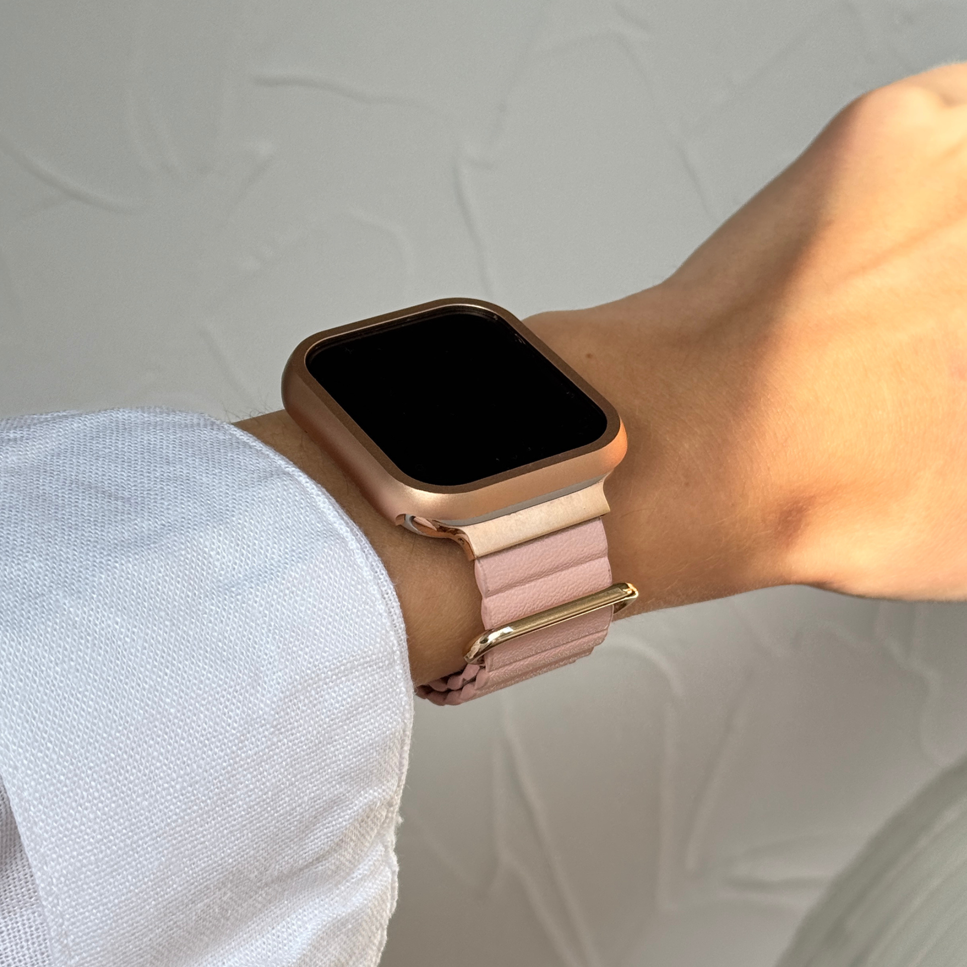 Rose gold stainless steel Apple Watch case cover worn on a wrist with a soft pink band. Premium protective bumper, available for Apple Watch 38mm to 49mm, Series 1-11, SE and Ultra