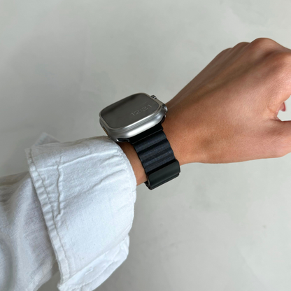 Black ribbed vegan leather Apple Watch band worn on a wrist with a crisp linen sleeve. Magnetic iWatch strap with a hidden magnet closure, compatible with Apple Watch 38mm to 49mm, Series 1-11, SE and Ultra