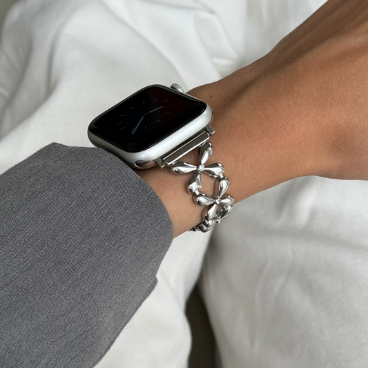 Silver floral link Apple Watch band worn on a wrist with a grey sleeve, metal strap for Apple Watch 38mm to 49mm
