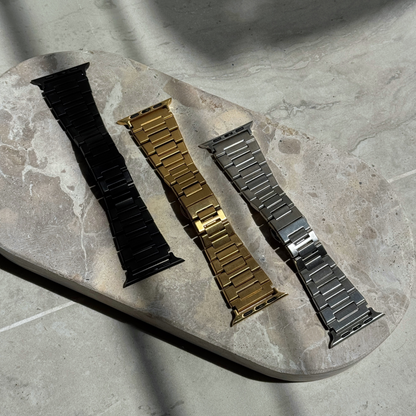 Black, gold and silver link Apple Watch bands laid out on a stone tray. Waterproof stainless steel iWatch straps, compatible with Apple Watch 38mm to 49mm, Series 1-11, SE and Ultra