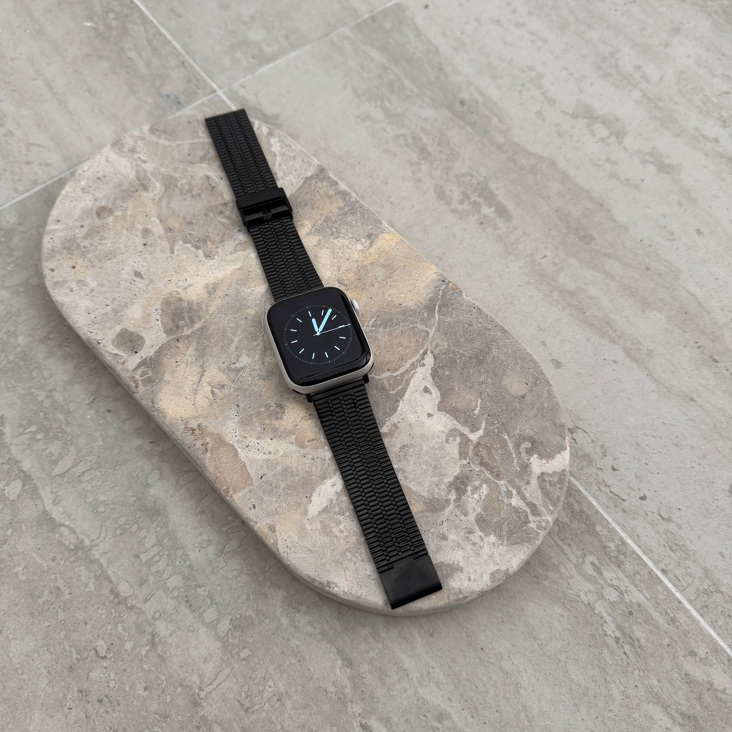 Black flat woven Apple Watch band lying flat on a stone tray. Lightweight stainless steel iWatch strap, compatible with Apple Watch 38mm to 49mm, Series 1-11, SE and Ultra
