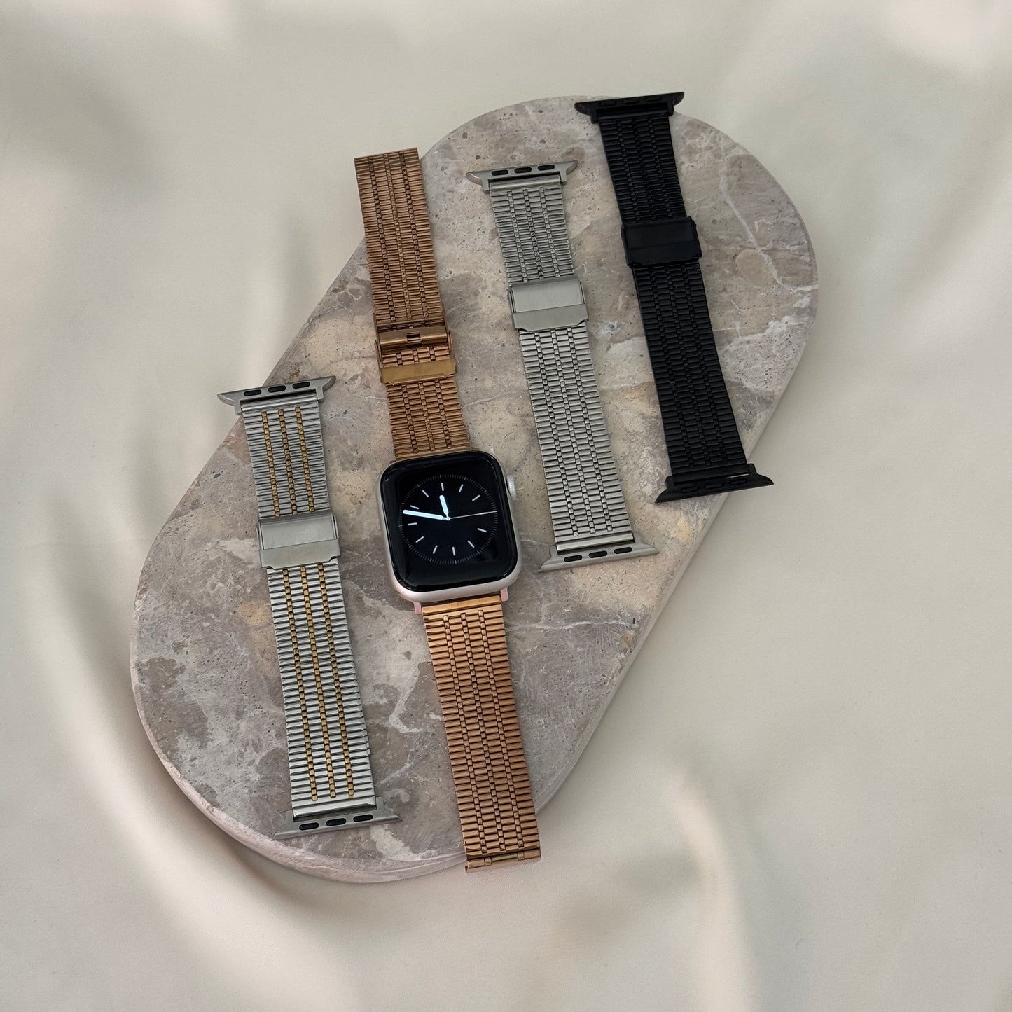 Silver gold, rose gold, silver and black flat woven Apple Watch bands laid on a stone tray. Unisex stainless steel iWatch straps, compatible with Apple Watch 38mm to 49mm, Series 1-11, SE and Ultra