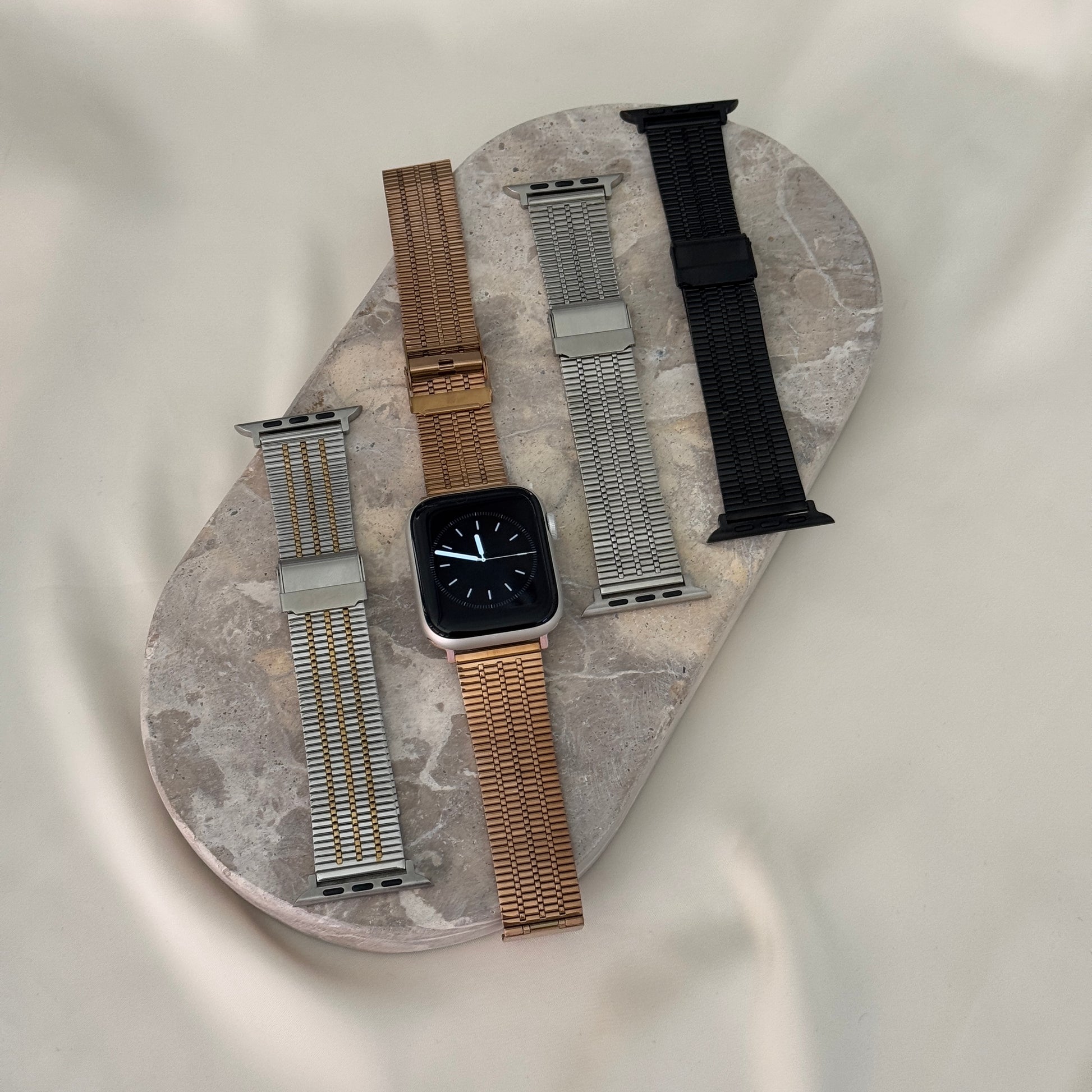 Silver gold, rose gold, silver and black flat woven Apple Watch bands laid on a stone tray. Unisex stainless steel iWatch straps, compatible with Apple Watch 38mm to 49mm, Series 1-11, SE and Ultra