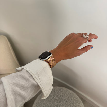 Rose gold flat woven Apple Watch band worn on a wrist with rings on the hand. Waterproof stainless steel iWatch strap, compatible with Apple Watch 38mm to 49mm, Series 1-11, SE and Ultra