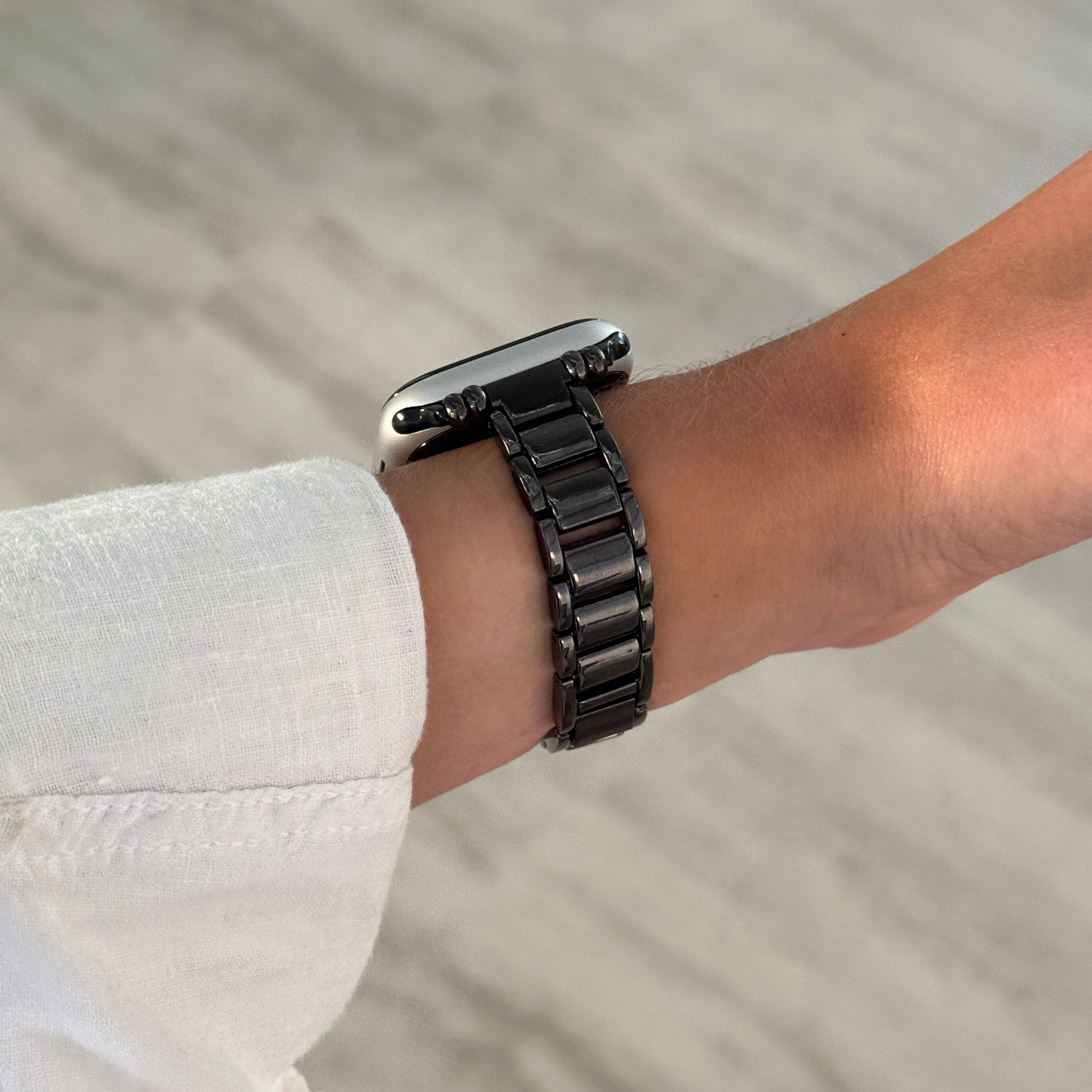 Black slim link Apple Watch band worn on a wrist with a white linen cuff. Slim metal iWatch bracelet with a clean modern aesthetic, compatible with Apple Watch 38mm to 49mm, Series 1-11, SE and Ultra