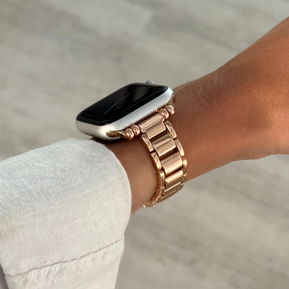 Rose gold slim link Apple Watch band worn on a wrist with a white linen cuff. Slim lightweight metal iWatch bracelet with a polished finish, compatible with Apple Watch 38mm, 40mm, 41mm, 42mm, 44mm, 45mm, 46mm and 49mm, Series 1-11, SE and Ultra