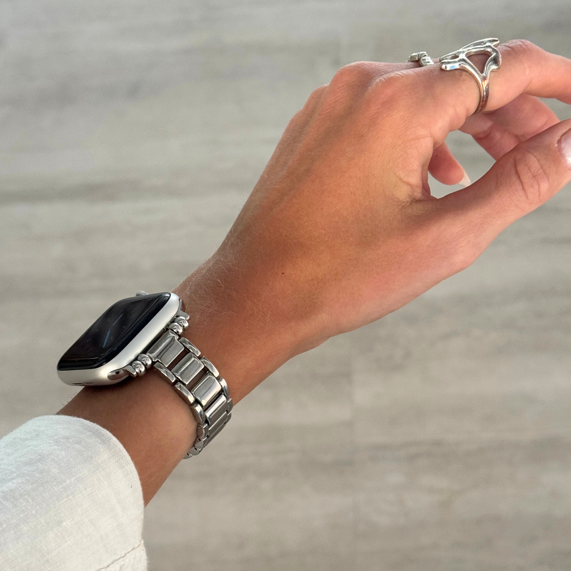 Silver slim link Apple Watch band worn on a wrist with rings on the hand. Lightweight metal iWatch bracelet with a polished finish, compatible with Apple Watch 38mm to 49mm, Series 1-11, SE and Ultra