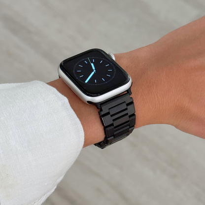Black link Apple Watch band worn on a wrist with a white linen cuff. Sleek stainless steel iWatch strap for everyday wear, compatible with Apple Watch 38mm to 49mm, Series 1-11, SE and Ultra