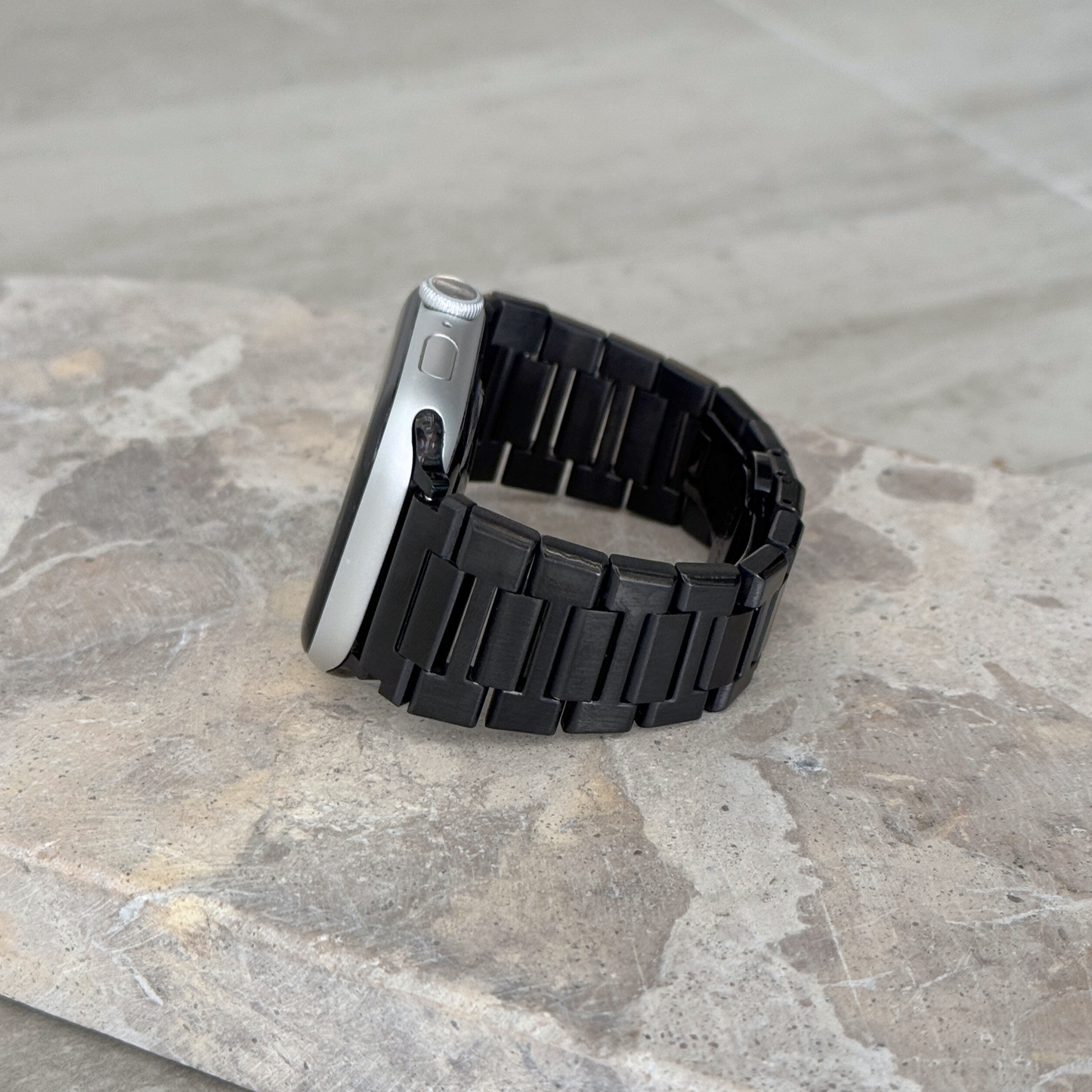 Black link Apple Watch band propped upright on a stone surface. Sleek unisex stainless steel iWatch strap, compatible with Apple Watch 38mm to 49mm, Series 1-11, SE and Ultra