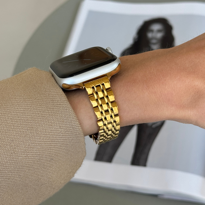 Gold woven link Apple Watch band worn with a camel sleeve beside a magazine, stainless steel strap for Apple Watch 38mm to 49mm