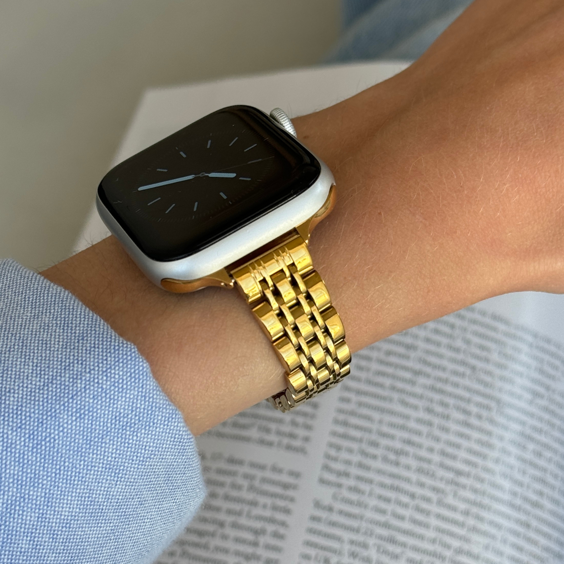 Gold woven link Apple Watch band worn on a wrist with a blue shirt cuff, stainless steel bracelet for Apple Watch 38mm to 49mm