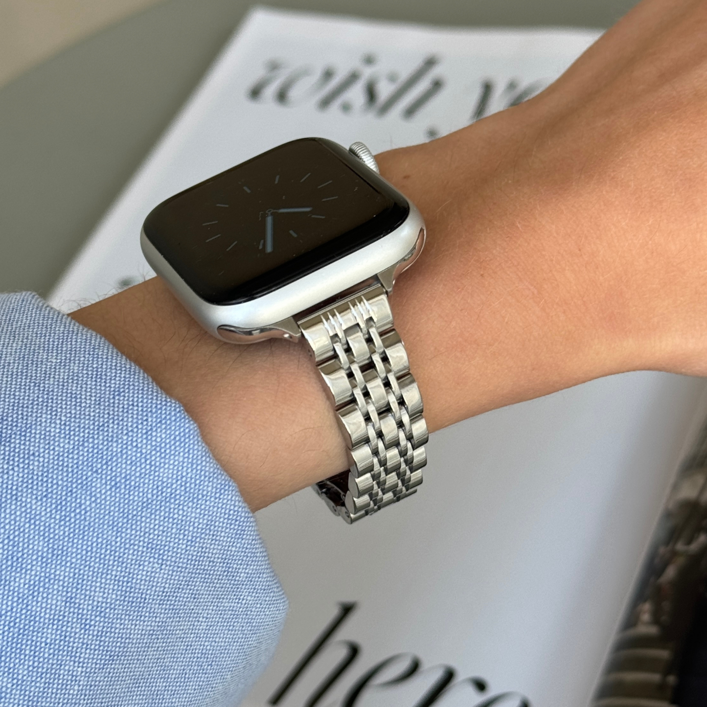 Silver woven link Apple Watch band worn on a wrist with a blue shirt cuff, stainless steel bracelet for Apple Watch 38mm to 49mm