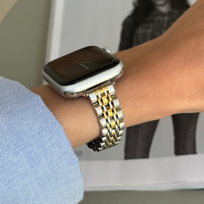 Silver gold woven link Apple Watch band worn with a blue sleeve beside a magazine, stainless steel strap for Apple Watch 38mm to 49mm