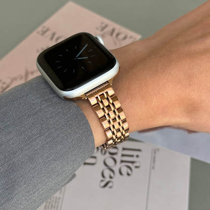 Rose gold woven link Apple Watch band worn with a grey sleeve over a printed page, stainless steel strap for Apple Watch 38mm to 49mm