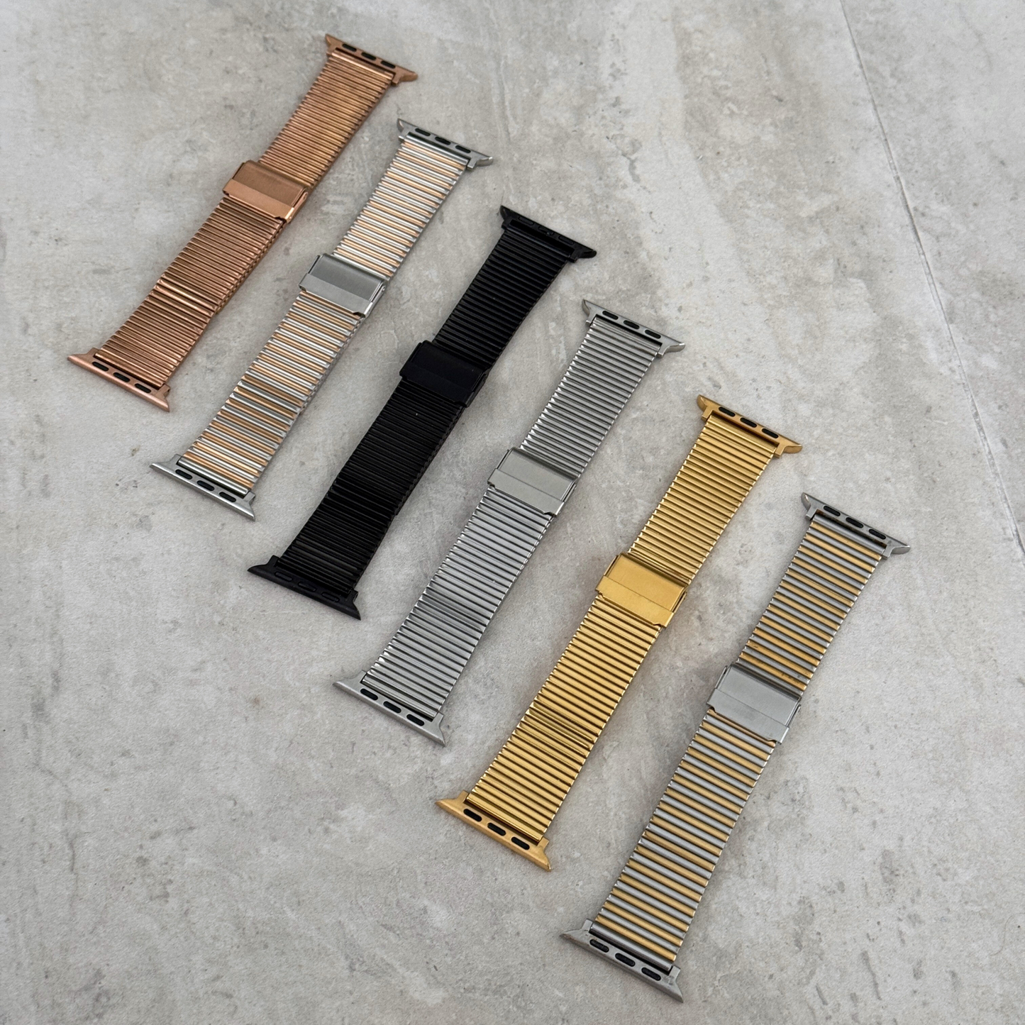 Rose gold, black, silver and gold ribbed loop Apple Watch bands laid out on concrete. Waterproof stainless steel iWatch straps, compatible with Apple Watch 38mm to 49mm, Series 1-11, SE and Ultra