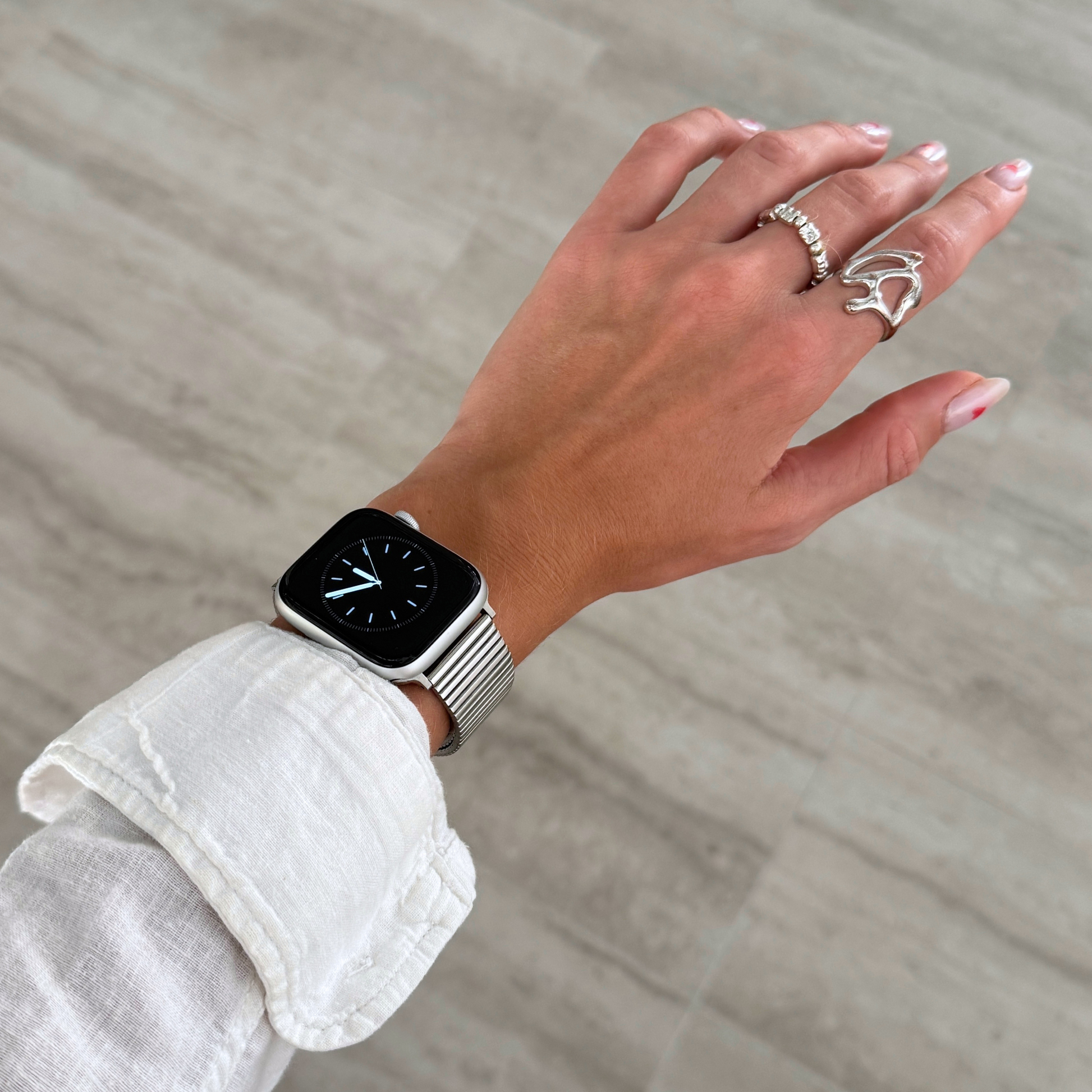 Silver ribbed loop Apple Watch band worn on a wrist with stacked rings. Stainless steel iWatch bracelet with a chic loop design, compatible with Apple Watch 38mm to 49mm, Series 1-11, SE and Ultra
