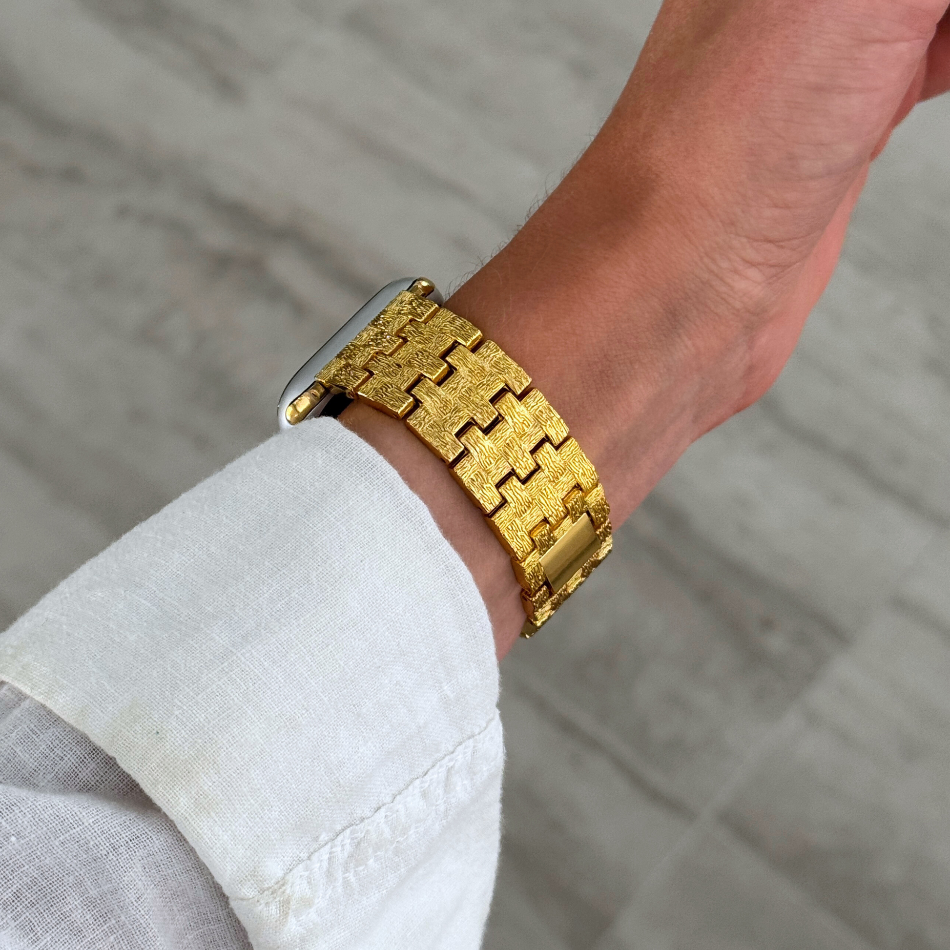 Gold baroque pattern Apple Watch band shown close up over a white linen sleeve. Luxurious metal iWatch armband with an intricate pattern, compatible with Apple Watch 38mm to 49mm, Series 1-11, SE and Ultra