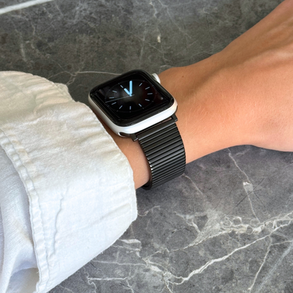 Black ribbed loop Apple Watch band worn on a wrist above grey marble. Stainless steel iWatch bracelet with a chic loop design, compatible with Apple Watch 38mm to 49mm, Series 1-11, SE and Ultra