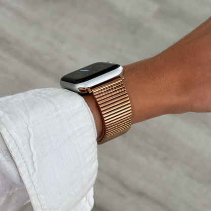 Rose gold ribbed loop Apple Watch band worn on a wrist with a white linen sleeve. Chic stainless steel iWatch strap for a perfect fit, compatible with Apple Watch 38mm to 49mm, Series 1-11, SE and Ultra
