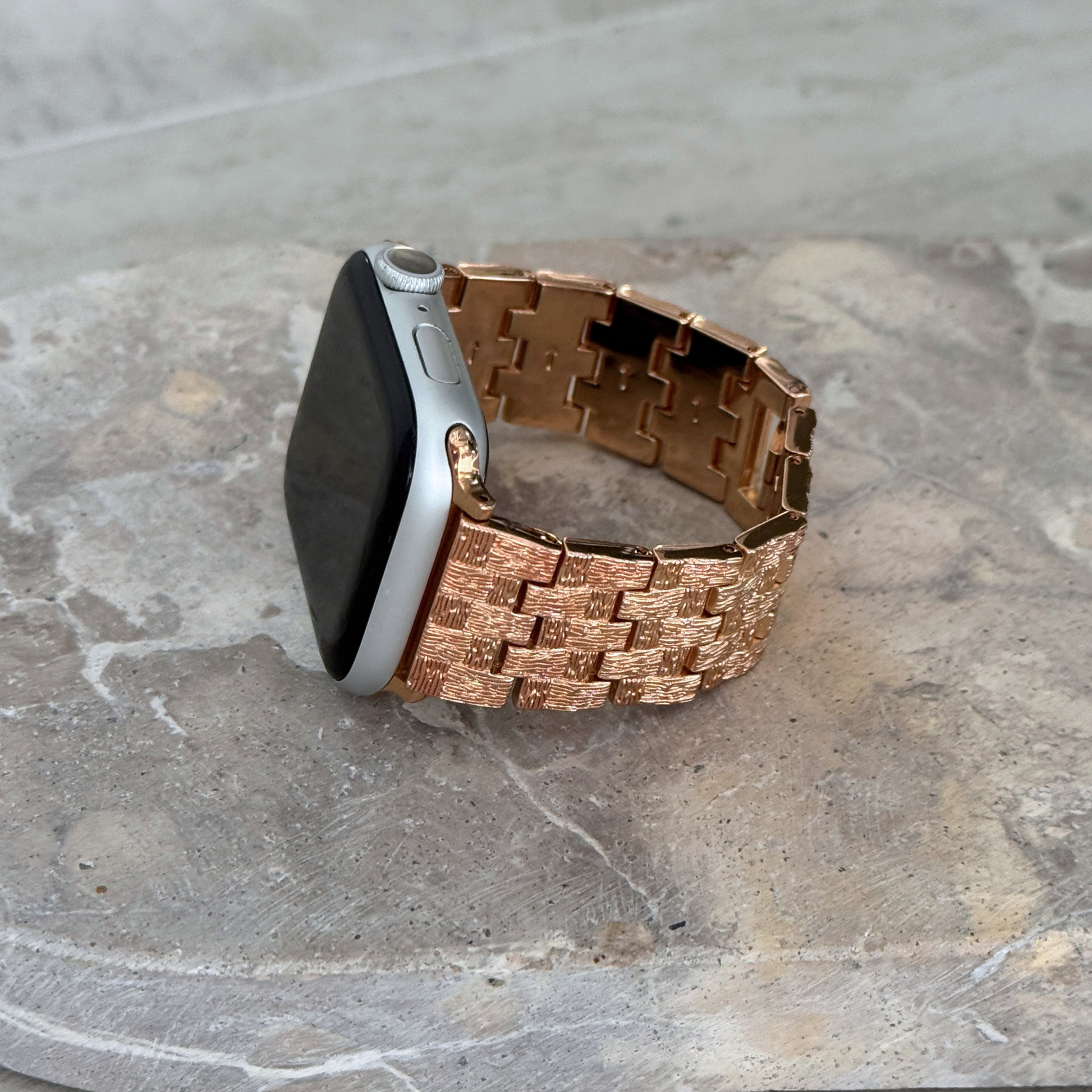 Rose gold baroque pattern Apple Watch band propped upright on a stone surface. Vintage inspired metal iWatch bracelet, compatible with Apple Watch 38mm to 49mm, Series 1-11, SE and Ultra