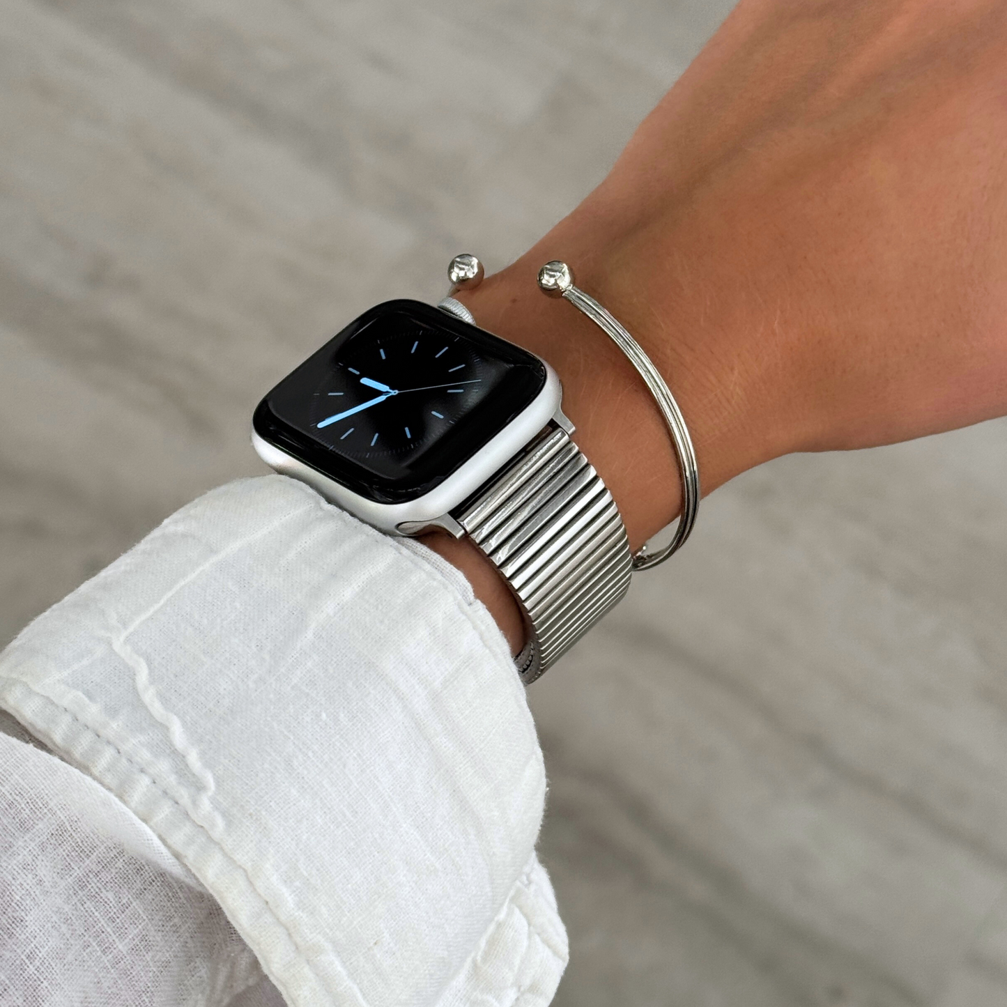 Silver ribbed loop Apple Watch band worn beside a thin cuff bangle. Waterproof stainless steel iWatch strap, easy to resize, compatible with Apple Watch 38mm to 49mm, Series 1-11, SE and Ultra
