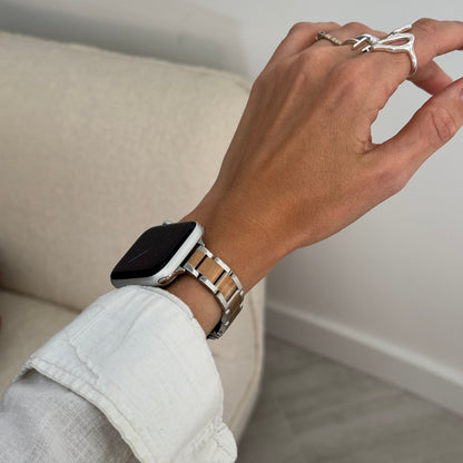 Silver rose gold slim link Apple Watch band worn with a white linen cuff beside a cream sofa, stainless steel strap for Apple Watch 38mm to 49mm