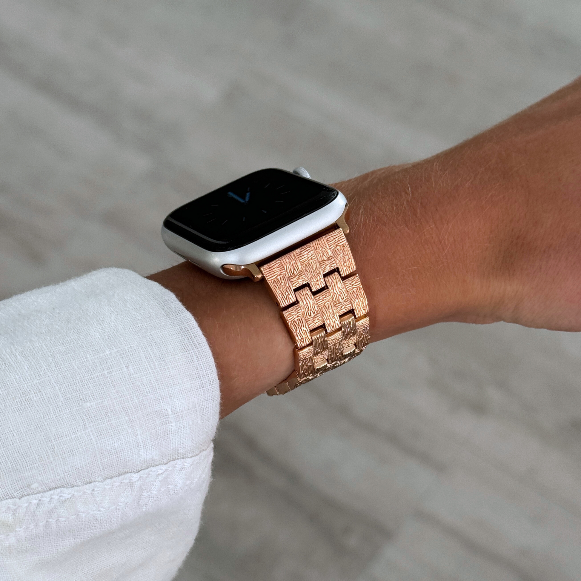 Rose gold baroque pattern Apple Watch band worn on a wrist with a white linen cuff. Luxurious metal iWatch bracelet with an intricate pattern, compatible with Apple Watch 38mm to 49mm, Series 1-11, SE and Ultra