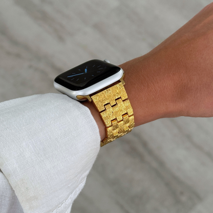 Gold baroque pattern Apple Watch band worn on a wrist with a white linen cuff. Vintage inspired metal iWatch bracelet, compatible with Apple Watch 38mm to 49mm, Series 1-11, SE and Ultra