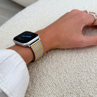 Silver gold ribbed loop Apple Watch band worn on a wrist resting on a boucle cushion. Waterproof stainless steel iWatch bracelet, compatible with Apple Watch 38mm to 49mm, Series 1-11, SE and Ultra