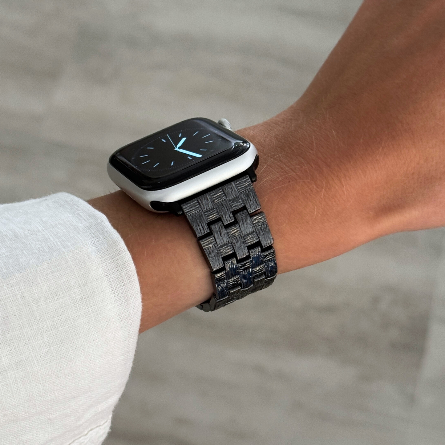 Black baroque pattern Apple Watch band worn on a wrist with a white linen cuff. Metal iWatch bracelet with brushed matte and polished shine, compatible with Apple Watch 38mm to 49mm, Series 1-11, SE and Ultra