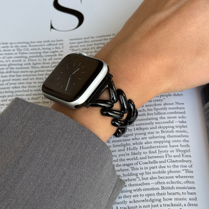 Black chunky chain Apple Watch band worn on a wrist above an open magazine. Metal iWatch bracelet that elevates any outfit, compatible with Apple Watch 38mm to 49mm, Series 1-11, SE and Ultra