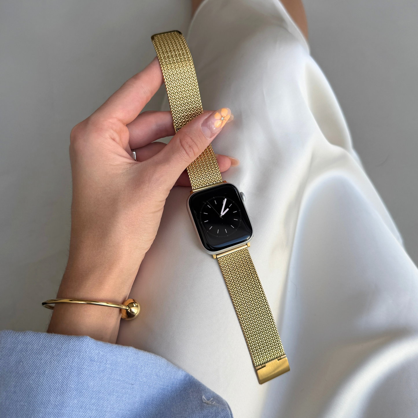 Gold mesh loop Apple Watch band held in a hand beside a gold bangle. Sleek stainless steel iWatch bracelet, compatible with Apple Watch 38mm to 49mm, Series 1-11, SE and Ultra