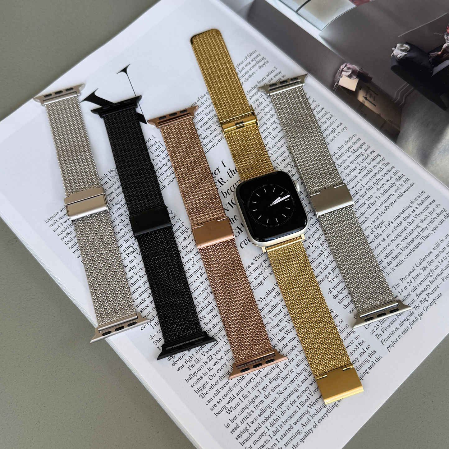 Starlight, black, rose gold, gold and silver mesh loop Apple Watch bands laid out on a magazine. Luxury stainless steel iWatch straps for women, compatible with Apple Watch 38mm to 49mm, Series 1-11, SE and Ultra