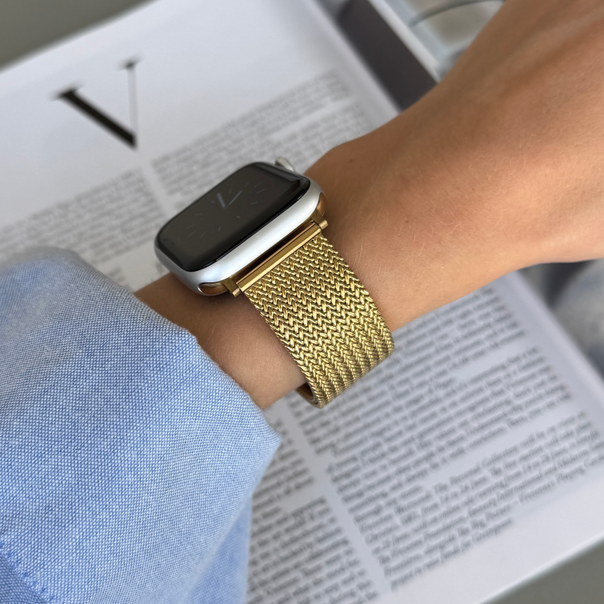 Gold mesh loop Apple Watch band worn on a wrist with a blue shirt cuff. Minimalist stainless steel iWatch bracelet, compatible with Apple Watch 38mm to 49mm, Series 1-11, SE and Ultra
