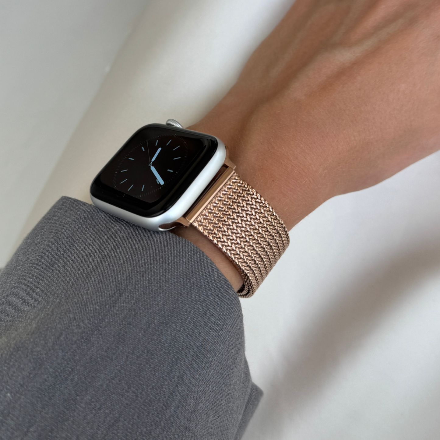 Rose gold mesh loop Apple Watch band worn on a wrist with a grey sleeve. Sleek stainless steel iWatch bracelet, compatible with Apple Watch 38mm to 49mm, Series 1-11, SE and Ultra