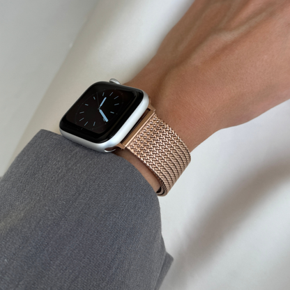 Rose gold mesh loop Apple Watch band worn on a wrist with a grey sleeve. Sleek stainless steel iWatch bracelet, compatible with Apple Watch 38mm to 49mm, Series 1-11, SE and Ultra