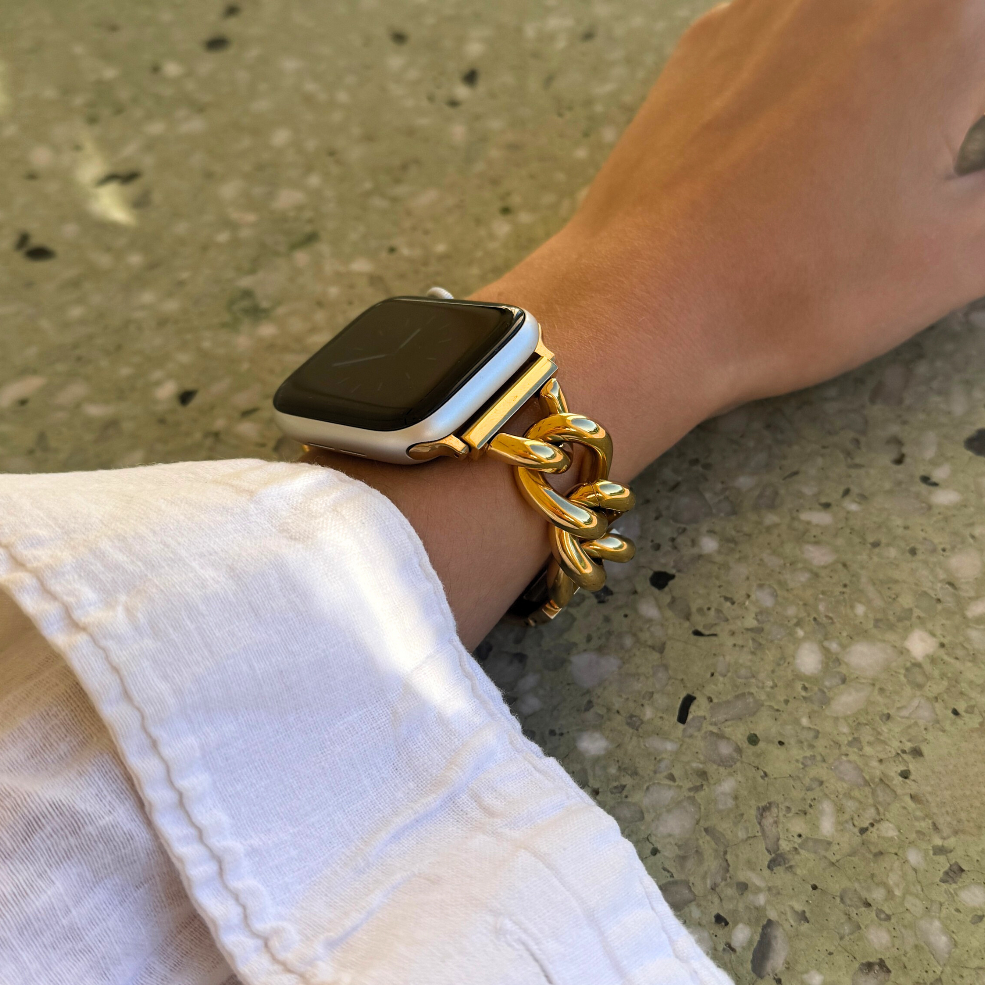 Gold chain link Apple Watch band worn on a wrist with a white linen cuff. Statement stainless steel iWatch strap that adds instant glam, compatible with Apple Watch 38mm to 49mm, Series 1-11, SE and Ultra