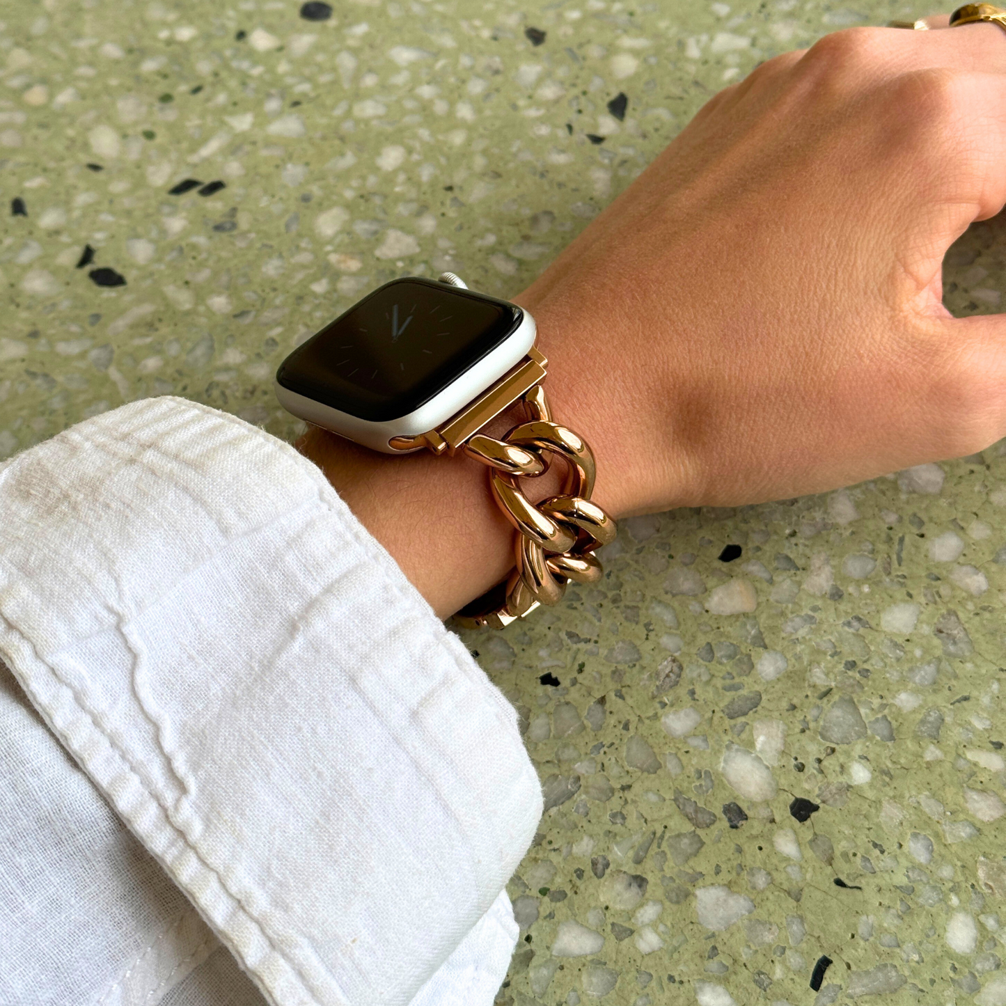 Chunky chain link Rose Gold Apple Watch band worn on a wrist with a white linen cuff outdoors. Statement stainless steel iWatch strap with oversized links, compatible with Apple Watch 38mm to 49mm, Series 1-11, SE and Ultra