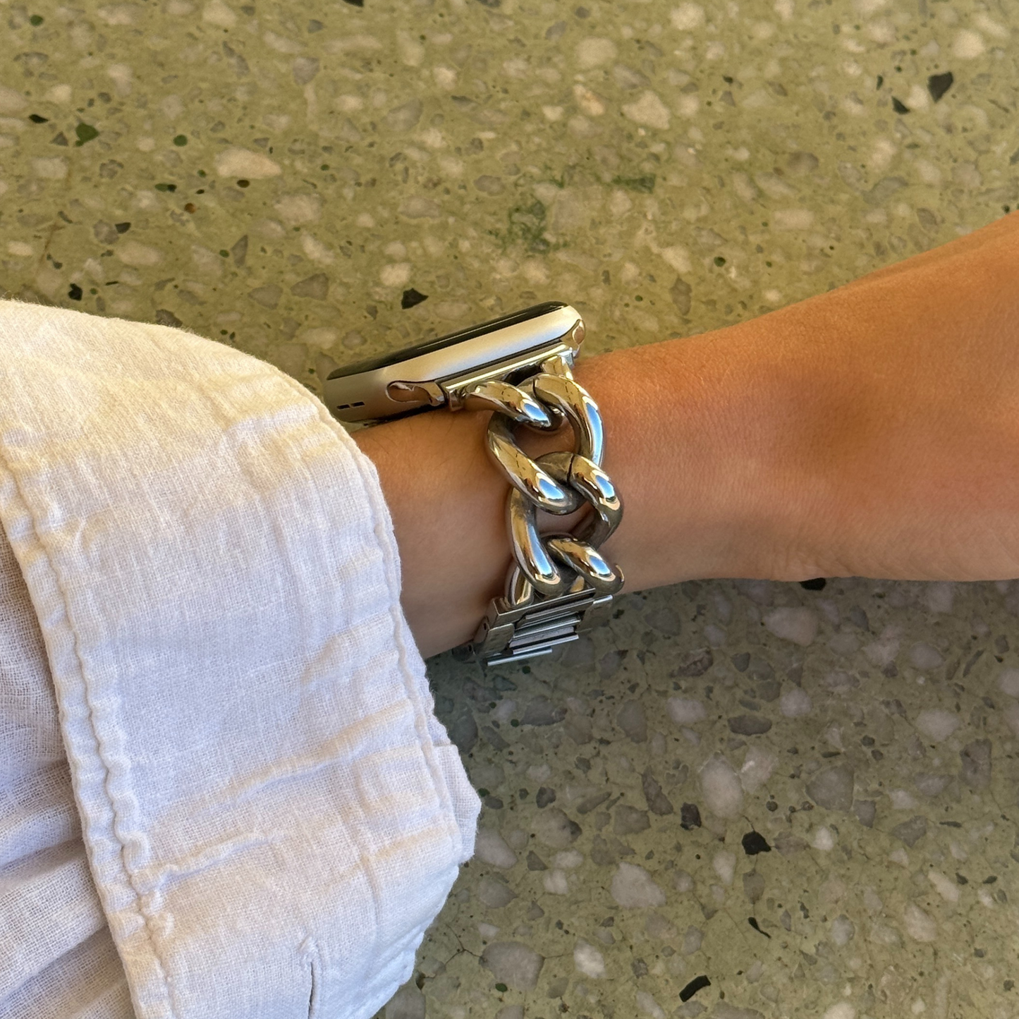 Silver chain link Apple Watch band worn on a wrist against a pale terrazzo wall. Waterproof stainless steel iWatch strap with oversized links, compatible with Apple Watch 38mm to 49mm, Series 1-11, SE and Ultra