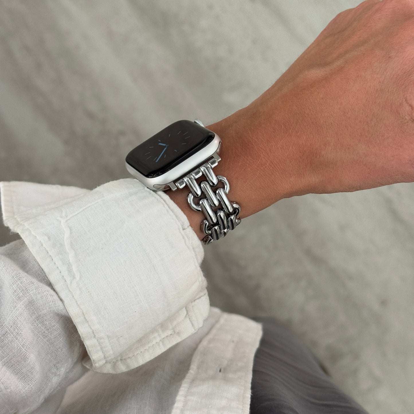 Silver chain link Apple Watch band worn on a wrist with a white linen cuff. Metal iWatch bracelet with a high polish shine, compatible with Apple Watch 38mm to 49mm, Series 1-11, SE and Ultra