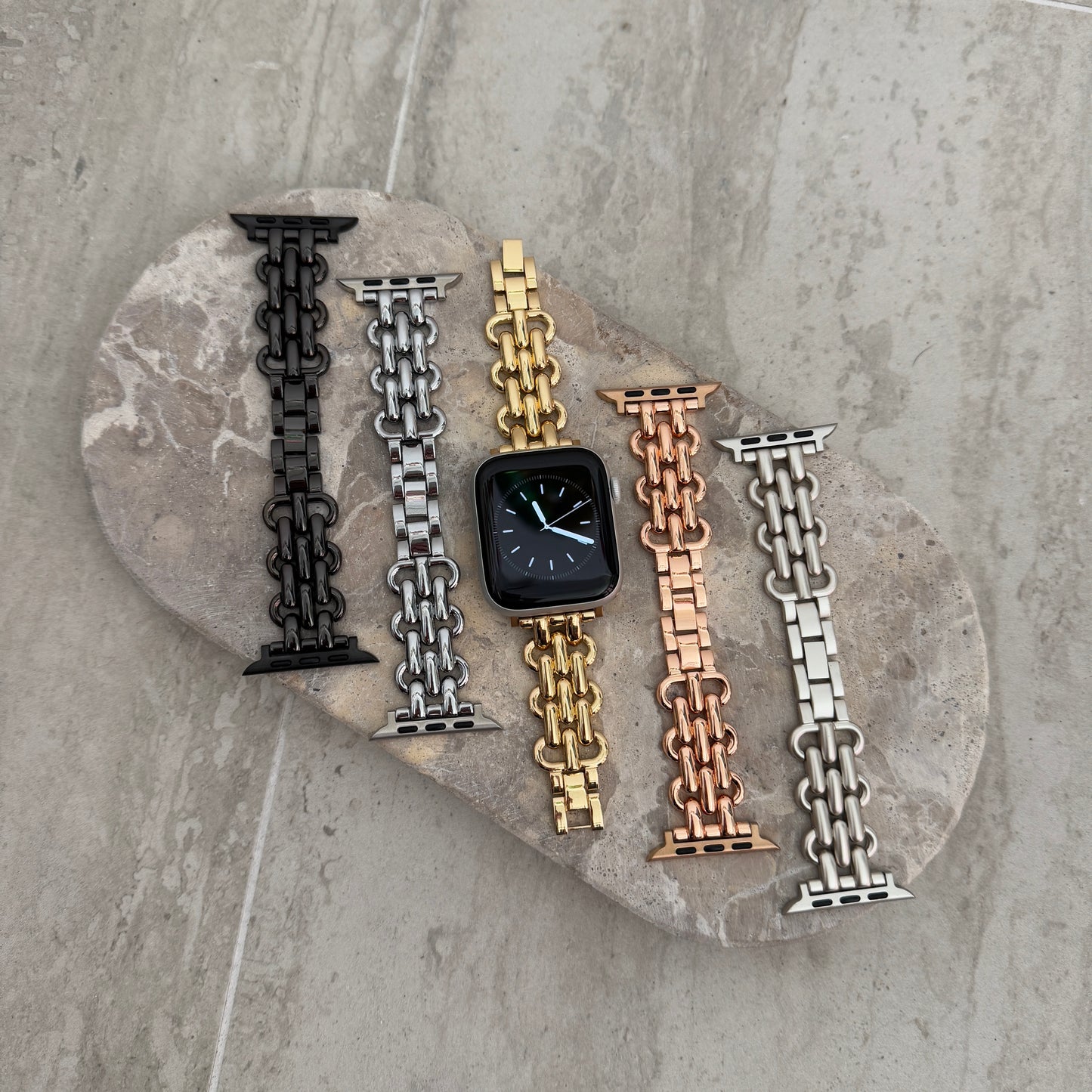 Black, silver, gold, rose gold and starlight chain link Apple Watch bands laid out on a stone tray. Sleek metal iWatch straps and bracelets, compatible with Apple Watch 38mm to 49mm, Series 1-11, SE and Ultra